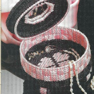 Può includere: Una scatola per gioielli in crochet nero e rosa con il coperchio aperto, che rivela una collana di perle, un anello e altri gioielli all'interno.