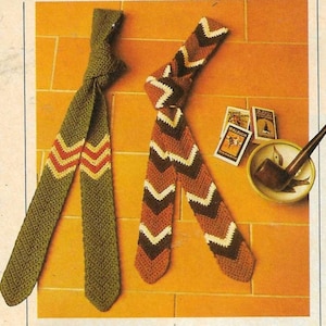 May include: Two crocheted neckties with chevron patterns. One is olive green with red and yellow accents, the other is brown with cream and dark brown chevrons. A pipe and small books are also visible.