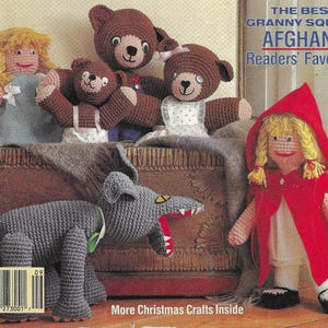 May include: A crocheted wolf with an open mouth, a crocheted red riding hood doll, and four crocheted bears. The bears are brown and white and are sitting on a wooden crate. The text "The Best Granny Square Afghans Readers' Favorite" is at the top of the image.
