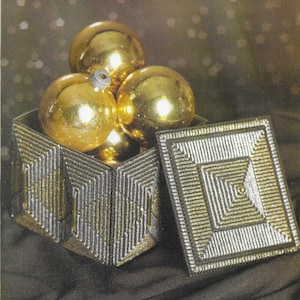 May include: A silver and gold decorative box with a lid. The box is filled with gold Christmas ornaments.