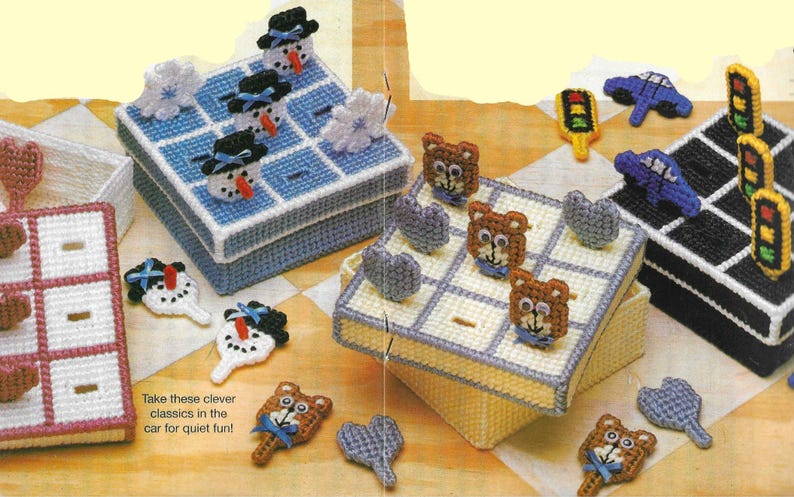 May include: Four colorful plastic canvas boxes with lids, each containing a different game. The games include tic-tac-toe with snowman pieces, tic-tac-toe with bear pieces, a car game with traffic light pieces, and a tic-tac-toe game with heart pieces. The text on the bottom of the image reads "Take these clever classics in the car for quiet fun!"