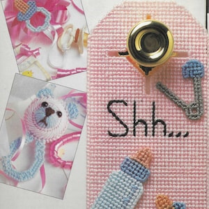 May include: A pink canvas door hanger with a blue and white teddy bear, a baby bottle, and a stethoscope. The text "Shh..." is embroidered on the door hanger.