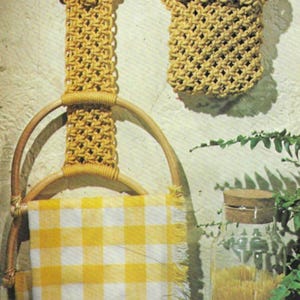 以下が含まれることがあります： 黄と白のチェック柄のタオルが付いたタオルホルダー、道具入れ、おろし金が特徴の、マクラメのキッチンセット。ベージュのマクラメと木材で作られており、素朴で手作りの美学を作り出しています。