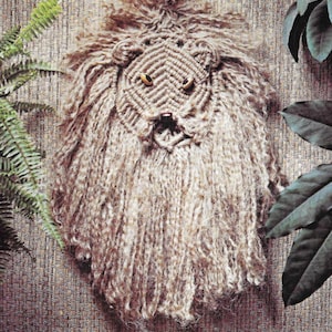 Pode incluir: Um pendurado de cabeça de leão marrom e branco com olhos dourados. A juba do leão é feita de fio e é muito fofa.