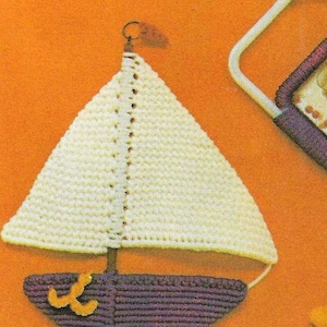 May include: A crocheted sailboat wall hanging with a white sail and a purple hull. The sailboat has a small anchor detail on the front.