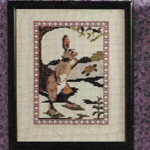 Peut inclure: Image d'une broderie au point de croix encadrée représentant un lapin dans un cadre naturel. L'œuvre utilise des tons de marron, beige et vert, avec une bordure décorative. Le lapin est près de l'eau, tenant une feuille.
