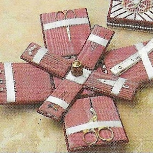 May include: A pink and white sewing kit containing a selection of tools, including scissors, needles, and a thimble. The kit is made of fabric and features a starburst design.