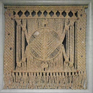 May include: A framed macrame wall hanging with a circular design in the centre. The macrame is made of natural coloured rope and has a fringe border.