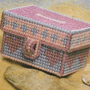 May include: A small, pink and blue plastic canvas box with a latch. The box is decorated with a geometric pattern.