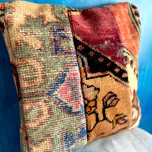 May include: A square pillow with a patchwork design made from different pieces of colorful fabric. The pillow is made from a variety of fabrics, including a green and blue fabric, a red and orange fabric, and a brown and black fabric.
