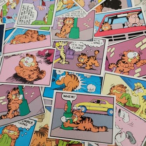 May include: A collection of Garfield comic strip panels. The panels feature the orange cat Garfield in various poses, with speech bubbles and text like "WHEW!" and "IT'S THE CLAWS". The panels have pink, blue, and yellow backgrounds.