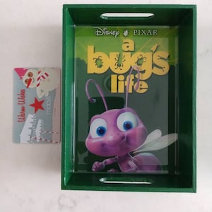 May include: A green wooden tray with a glass insert featuring a cartoon ant from the Disney Pixar movie "A Bug's Life". The tray has two handles on the sides.