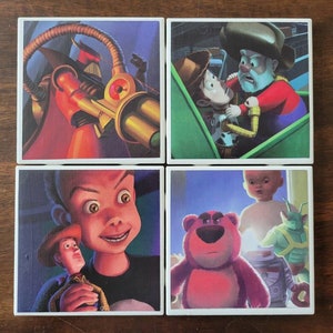 May include: Set of four square ceramic coasters featuring characters from the Toy Story franchise. The coasters feature a close-up of Buzz Lightyear's head, Woody and Buzz riding a roller coaster, a close-up of Sid's face, and a close-up of a teddy bear.