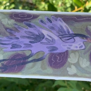 K&ouml;nnte beinhalten: Ein rechteckiger Aufkleber mit einer Illustration eines Vogels im Flug. Der Vogel ist &uuml;berwiegend lila mit dunkleren lila Akzenten und einem gelben Schnabel. Der Hintergrund zeigt lila Blumen- und Blattmotive.