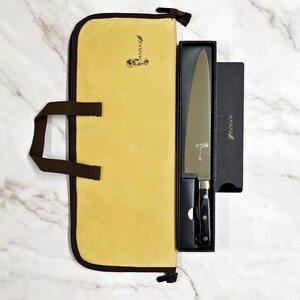 May include: A chef's knife with a black handle and silver blade, presented in a black box and a yellow carrying case. The knife and case have the brand name "HANAKO" printed on them. The carrying case has a brown handle.