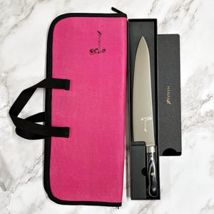 May include: A chef's knife with a silver blade and a black and gray handle, presented in a black box and a pink carrying case. The knife and case have the brand name "HANAKO" printed on them.