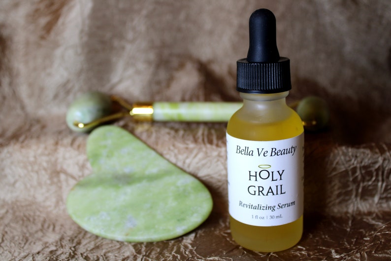 Puede incluir: Una botella de vidrio transparente con un gotero negro y una etiqueta blanca que dice "Bella Ve Beauty HOLY GRAIL Revitalizing Serum 1 fl oz | 30 ml."