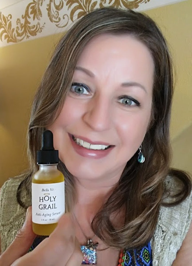 Puede incluir: Una mujer sostiene una peque&ntilde;a botella de vidrio &aacute;mbar con un gotero. La etiqueta de la botella dice "Bella Ve Holy Grail Anti-Aging Serum 1 fl oz (30 ml)".