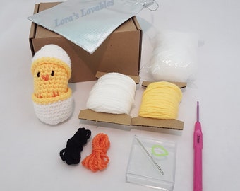 May include: A crochet chick in an egg kit with white, yellow, and orange yarn, black and orange embroidery floss, a crochet hook, a needle, a plastic container, and a white drawstring bag labeled "Lora's Lovables".
