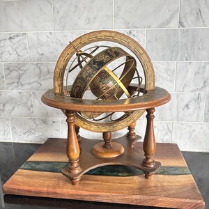 May include: An antique armillary sphere, featuring a detailed globe and brass rings, set on a wooden stand. The sphere displays intricate designs and text, reflecting a vintage style. The stand is made of dark wood and has a decorative base.