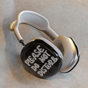 Puede incluir: Auriculares blancos y negros con el texto "PLEASE DO NOT DISTURB" impreso en una orejera.