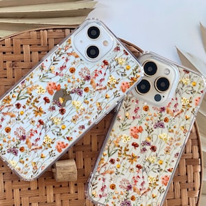 May include: Two clear phone cases with a floral design. The cases are made with real pressed flowers and have a white background with red, orange, and yellow flowers.