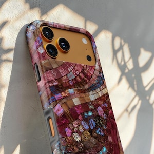 May include: A smartphone case featuring a mosaic pattern of iridescent, multi-colored shell tiles in shades of deep magenta, purple, and gold. The case has a gold-toned camera housing with three circular lenses and a flash, and a grey side button.