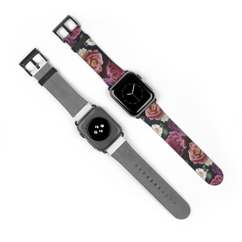 May include: Two Apple Watch bands, one with a floral print and one with a gray leather strap. The floral band features a dark background with pink, white, and purple flowers.