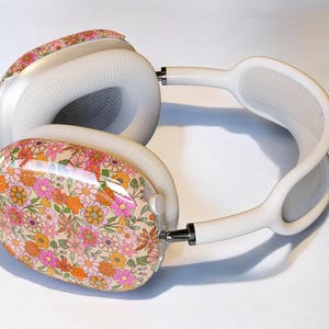 May include: White headphones with a floral pattern on the earcups. The floral pattern is pink, orange, and yellow.