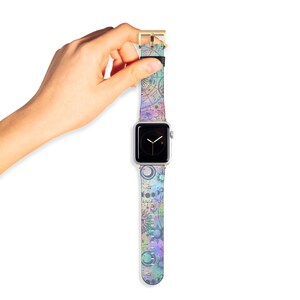K&ouml;nnte beinhalten: Eine Smartwatch mit rechteckigem silbernem Geh&auml;use und schwarzem Digitaldisplay sowie einem pastellfarbenen Armband. Das Armband zeigt ein himmlisches Muster mit Monden, Sternen und Tierkreiszeichen in den Farben Violett, Blau, Gr&uuml;n und Pink.