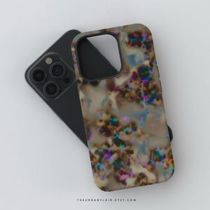 Könnte beinhalten: Smartphone-Hülle mit einem abstrakten Design. Die Hülle hat ein wirbelndes Muster aus Braun, Beige und schillernden Farben, darunter Blau, Lila und Grün. Die Handyhülle liegt auf einem schwarzen Smartphone.