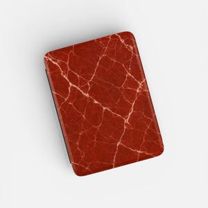 May include: A rectangular, red case with a marble-like pattern. The case has a textured surface with white vein-like lines running across it. The edges of the case are black.