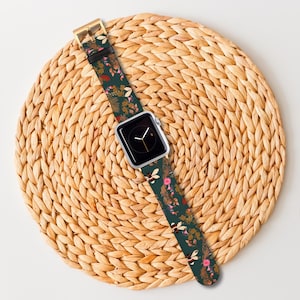 May include: A green watch strap with a floral and bee pattern. The strap is wrapped around a woven straw placemat.