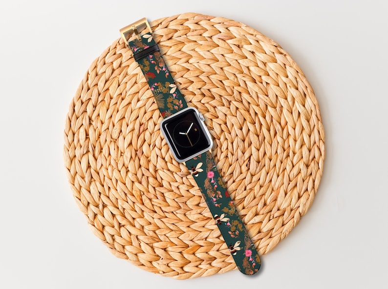 May include: A green watch strap with a floral and bee pattern. The strap is wrapped around a woven straw placemat.
