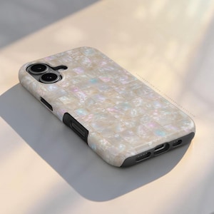 May include: A protective phone case featuring a grid of iridescent, pearlescent square tiles in shades of cream and white. The case has a black frame with cutouts for the camera lenses, side buttons, and charging port. Text reads THEURBANFLAIR.COM.