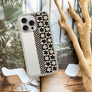 May include: A clear phone case with a black and white checkered pattern and a row of white flowers on a beige background.