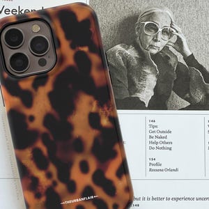 May include: A smartphone case featuring a brown and black tortoiseshell pattern with a triple camera cutout at the top. The bottom of the case displays the white text THEURBANFLAIR. The design covers the back of the device with a glossy finish.