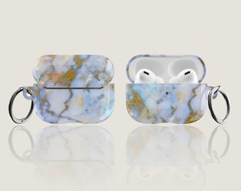 Może przedstawiać: Etui na AirPods w kolorze białym i złotym z marmurowym wzorem i srebrnym brelokiem. Etui jest otwarte, a AirPods są widoczne w środku.