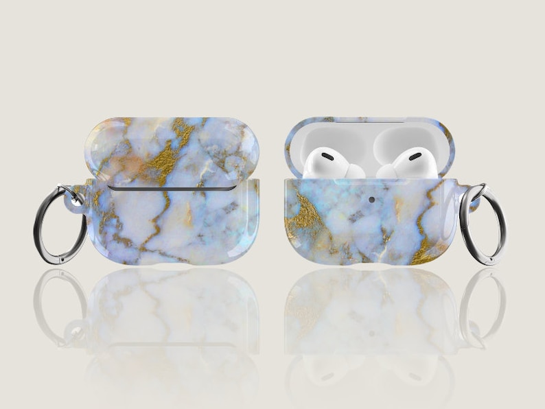 May include: A white and gold marble patterned case for AirPods with a silver keychain attached. The case is open and the AirPods are visible inside.