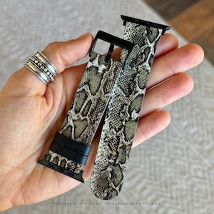 May include: A watch strap featuring a grey, black, and white snakeskin pattern. The strap includes black hardware, including a buckle and connectors. The text THEURBANFLAIR.COM - THEURBANFLAIR.ETSY.COM is printed in small letters at the bottom.