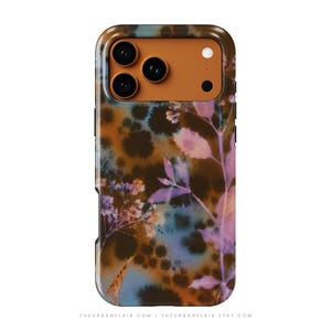 Puede incluir: Una funda para smartphone con un recorte rectangular para la c&aacute;mara y un panel naranja s&oacute;lido. La superficie trasera muestra un patr&oacute;n moteado en azul y marr&oacute;n oscuro superpuesto con un estampado bot&aacute;nico de tallos y hojas en color violeta claro. El texto THEURBANFLAIR.COM THEURBANFLAIR.ETSY.COM aparece en la parte inferior.