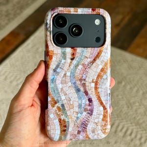 May include: A smartphone case featuring a mosaic pattern of wavy vertical lines in shades of peach, cream, light blue, and deep purple. The design consists of small, square-shaped tiles arranged in a flowing, multi-colored gradient across the back.