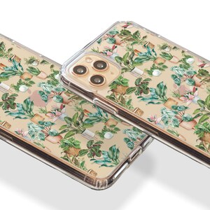 K&ouml;nnte beinhalten: Zwei transparente Handyh&uuml;llen mit beigefarbenem Hintergrund und einem Muster aus gr&uuml;nen und braunen Topfpflanzen. Die Handyh&uuml;llen sind f&uuml;r ein iPhone mit goldenem Kameraobjektiv.