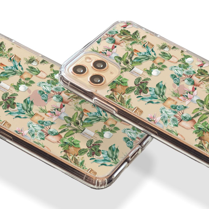 K&ouml;nnte beinhalten: Zwei transparente Handyh&uuml;llen mit beigefarbenem Hintergrund und einem Muster aus gr&uuml;nen und braunen Topfpflanzen. Die Handyh&uuml;llen sind f&uuml;r ein iPhone mit goldenem Kameraobjektiv.