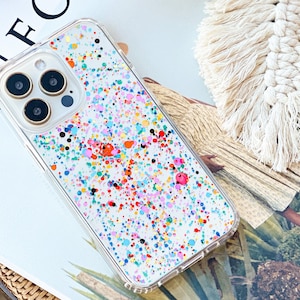 May include: A clear phone case with a white background and colorful paint splatters. The case has a raised camera bump with three black camera lenses.