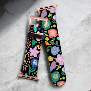 May include: Two colorful floral patterned Apple Watch bands with rose gold hardware. The bands are black with a variety of bright colors, including pink, blue, green, yellow, and orange.