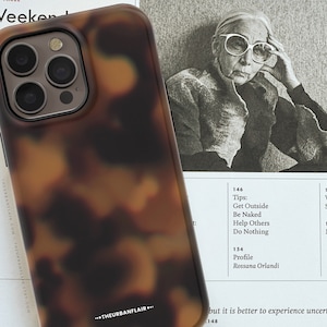 Może przedstawiać: Brązowe i czarne etui na telefon w stylu żółwim pancerzem z wycięciem na obiektyw aparatu. Etui leży na białym tle z tekstem w tle.