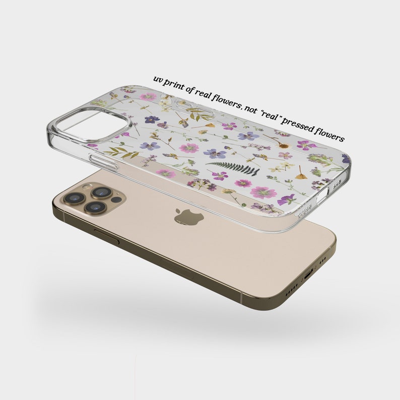 以下が含まれることがあります： 紫、ピンク、黄色などの花々がUVプリントされた透明な携帯電話ケース。ケースはゴールド色の携帯電話の上にあります。ケースのテキストは「uv print of real flowers, not 'real' pressed flowers」です。