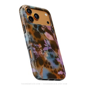 Puede incluir: Una funda para smartphone con un patr&oacute;n tie-dye marr&oacute;n y azul con siluetas florales p&uacute;rpuras superpuestas. El &aacute;rea de recorte de la c&aacute;mara es de color dorado met&aacute;lico. El texto THEURBANFLAIR.COM THEURBANFLAIR.ETSY.COM est&aacute; impreso en la parte inferior.