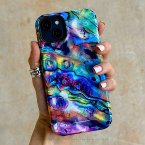 May include: A smartphone case featuring a vibrant, iridescent abalone shell pattern with swirling colors of deep blue, bright turquoise, magenta, and gold. The design has a glossy finish and includes a small black camera cutout at the top left corner.